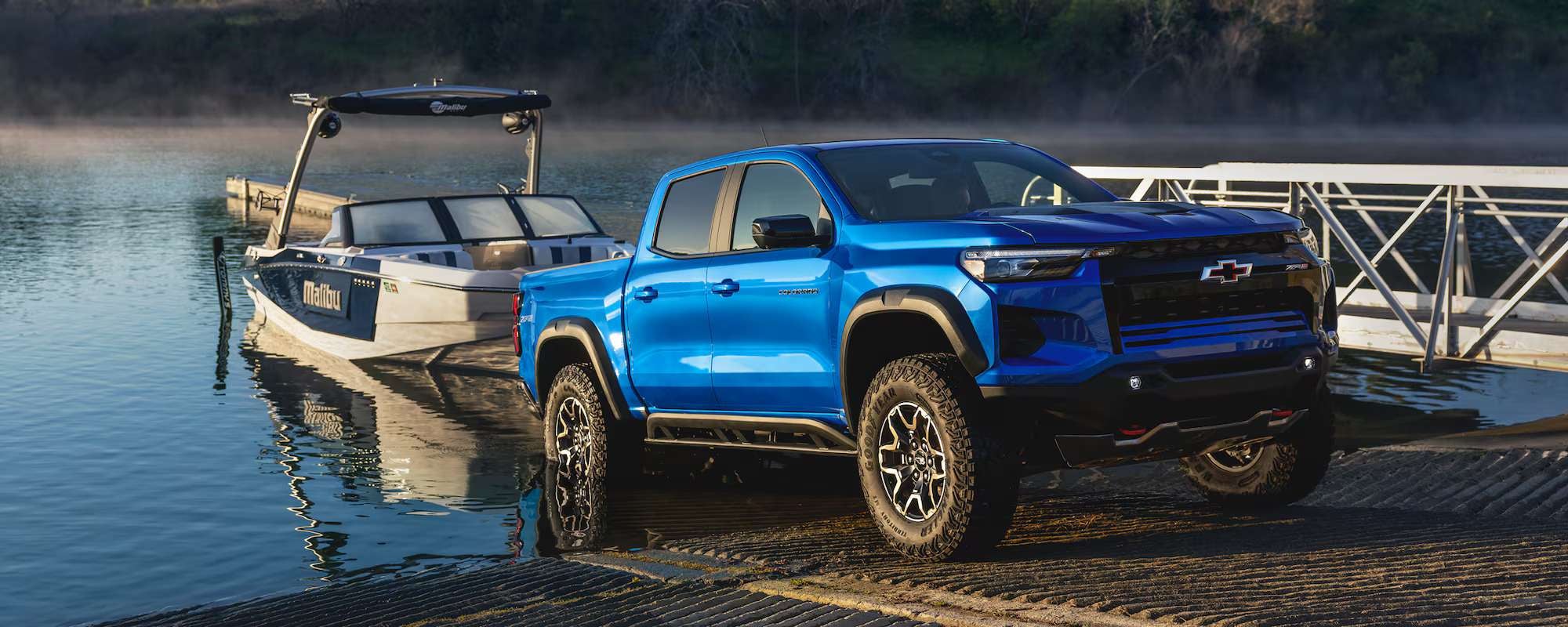 A blue 2026 Chevrolet Colorado 1500 pickup truck, consistently named among the top pickup trucks, towing a boat out of a lake.